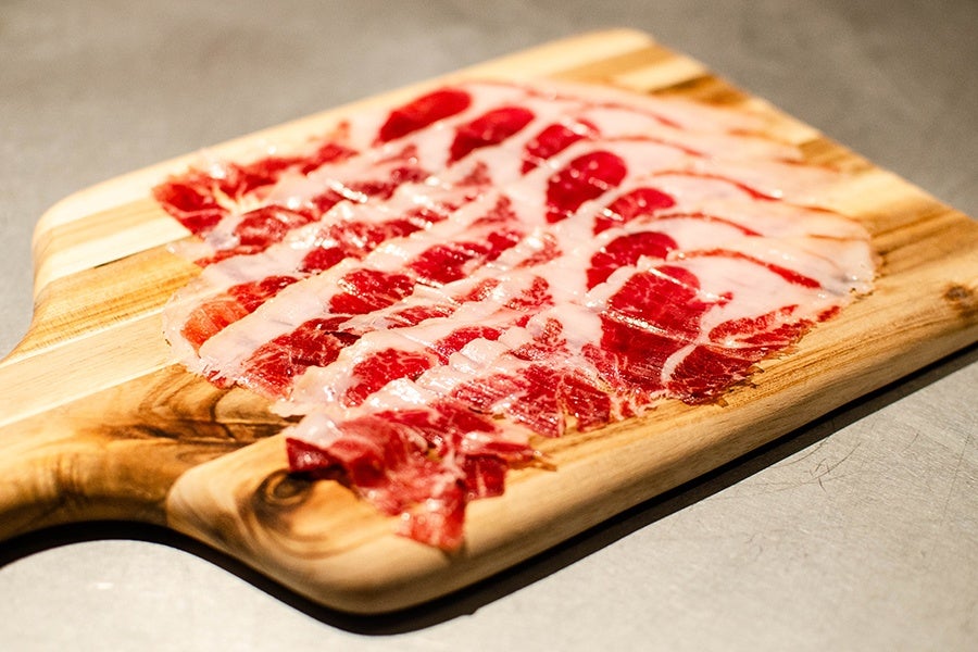 Thinly sliced, bright red ham is lined up on a wooden board.
