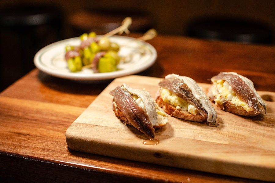 Anchovies sit on toast on a wooden board.