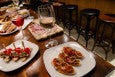 A spread of small Spanish bites and wine on a long wooden table with barstools in the background.