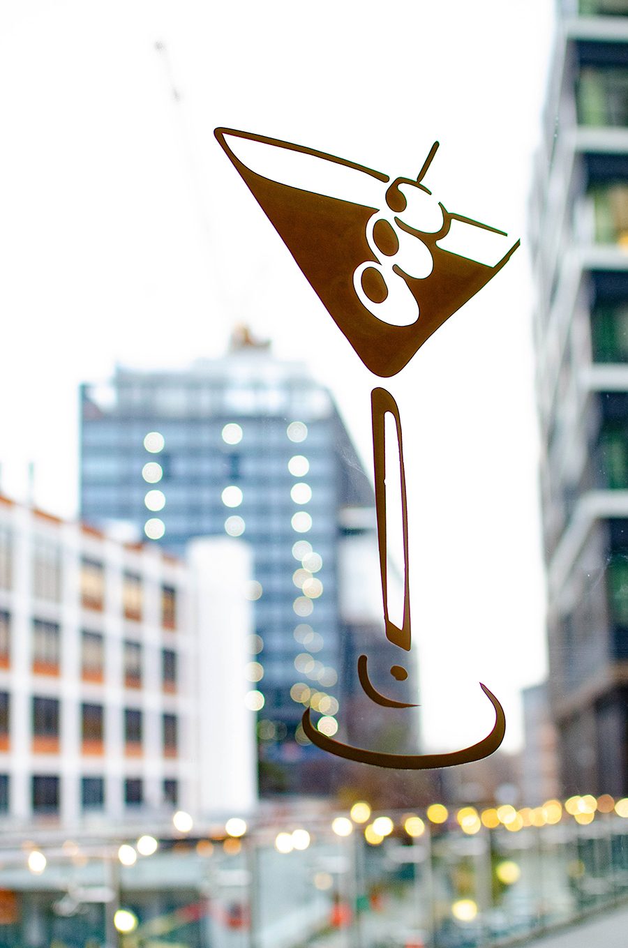 A martini glass decal is on a window, with tall city buildings visible outside.