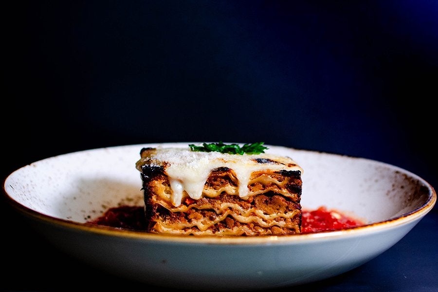 Lasagna with cheese melting on the top sits in a pool of tomato sauce in a shallow bowl.