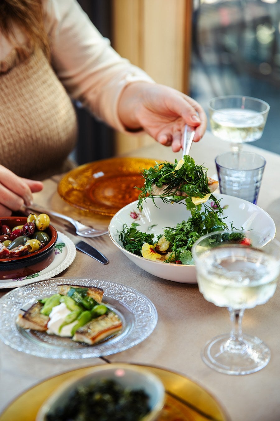 At a restaurant table, hands reach for a salad next to a bowl of olives.