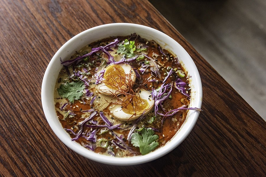 Overhead view of a ramen bowl with an egg, strips of red cabbage, and other toppings.
