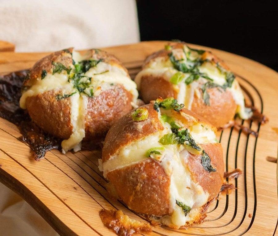 Three buns on a wooden board are split open to reveal creamy filling with green herbs on top.