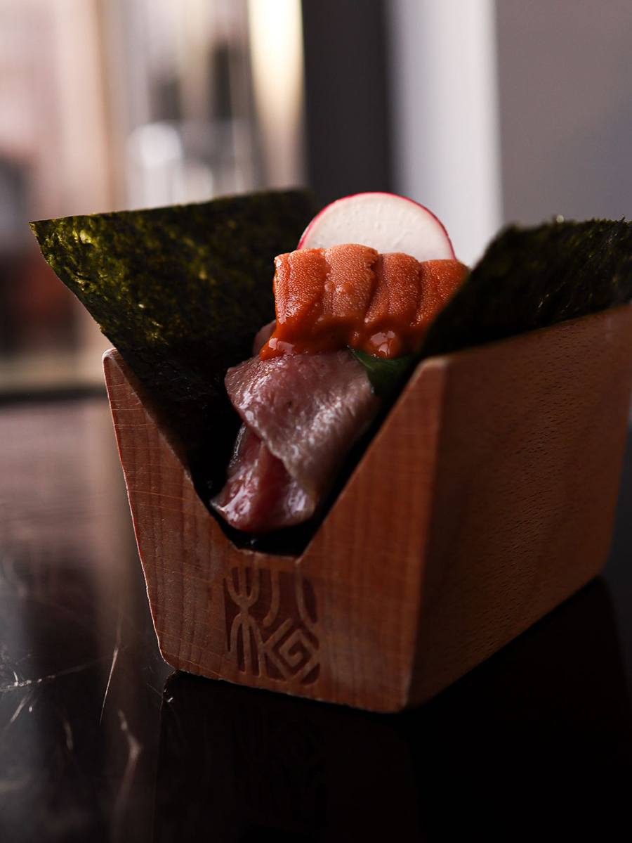 Seaweed is propped up in a V shape in a wooden holder, full of raw fish and a sliced radish.