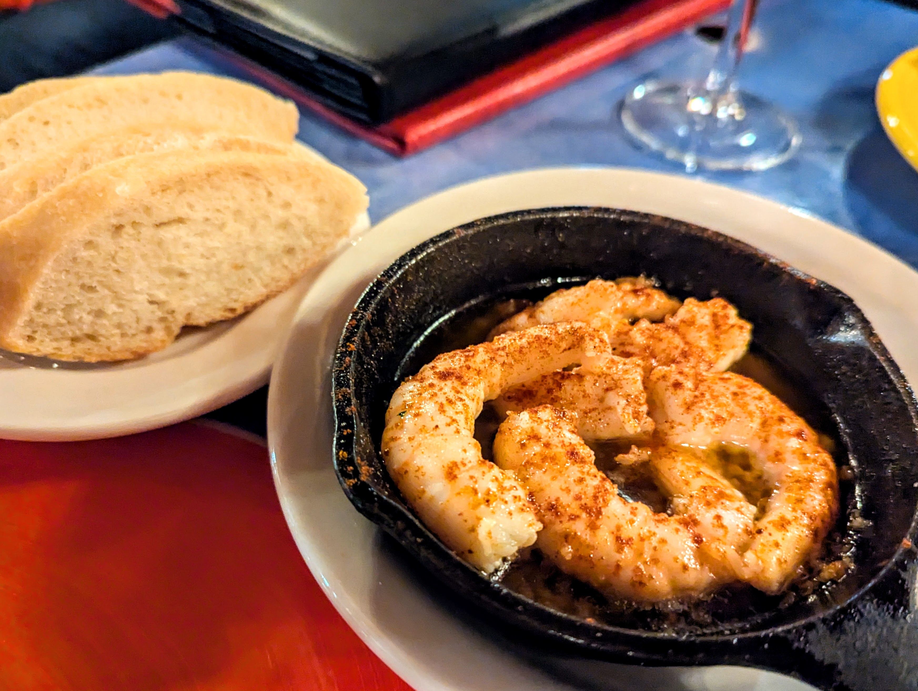 Shrimp dusted generously with red pepper are served in a tiny cast iron pan next to a plate of sliced white bread.