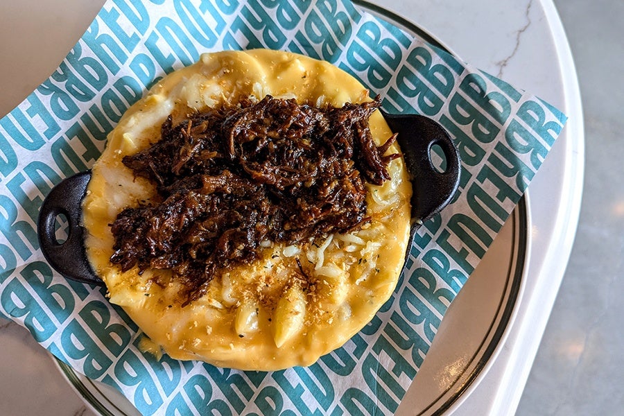 Overhead view of shells in a thick cheese sauce, topped with oxtail, in a cast-iron pan.