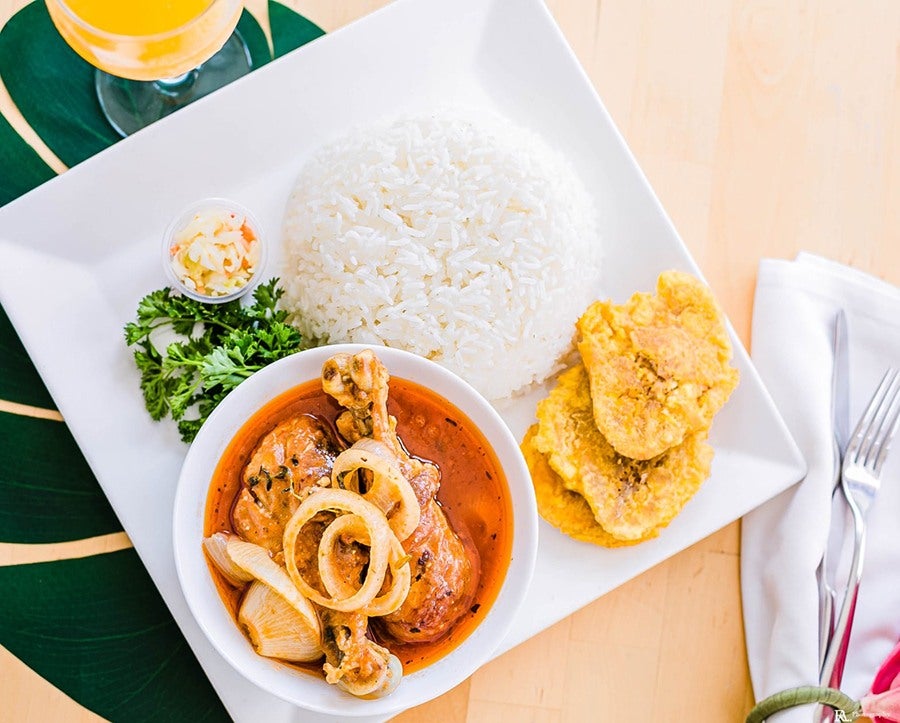 Overhead view of a Haitian chicken dish with rice, pikliz, and fried plantains on the side.