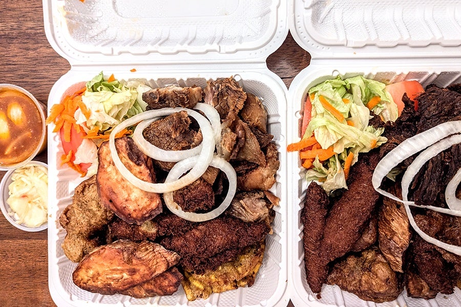 Overhead view of two takeout containers full of fried meat, fried sweet potato, fried plantain, fried malanga fritters, and a bit of salad.