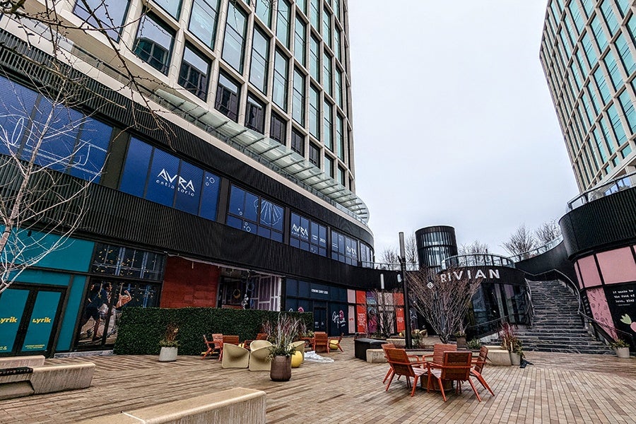 A courtyard spreads out between two tall city buildings, with two stories of retail and restaurant spaces under construction and papered over with posters announcing the incoming brands.