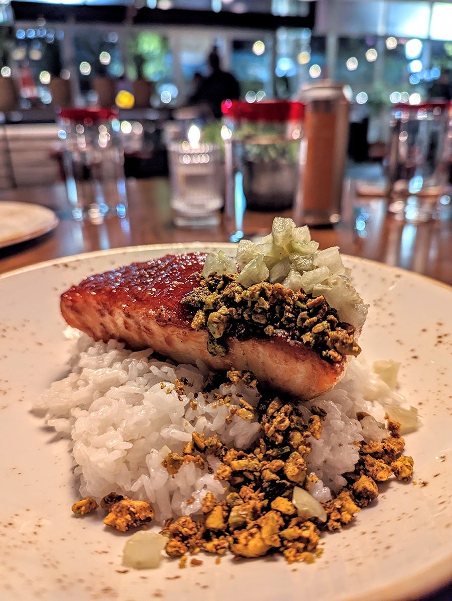 A salmon filet sits atop a pile of pistachio-garnished white rice on a restaurant table.