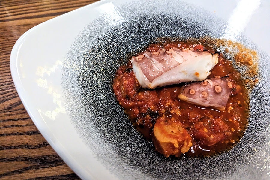 Grilled octopus sits in a pool of tomato sauce.