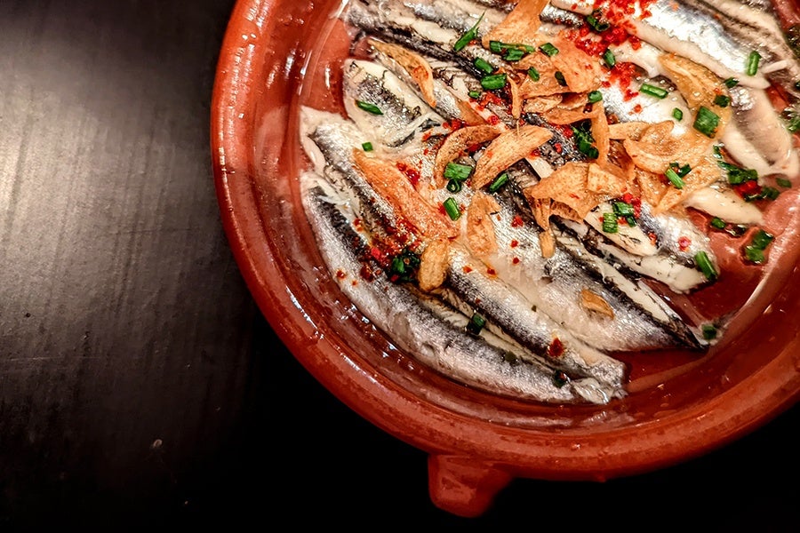 anchovies line a small red plate, topped with slivers of fried garlic