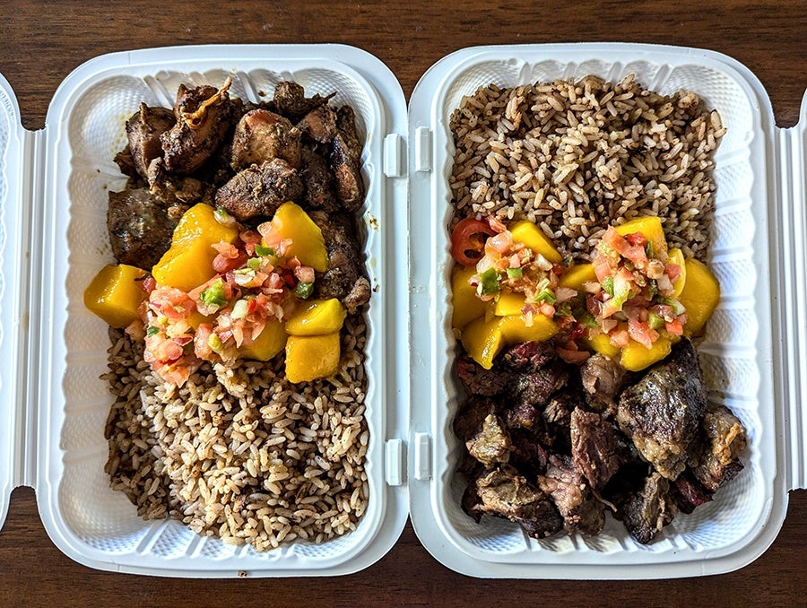 Overhead view of two takeout containers, one with chunks of spiced, grilled chicken, the other with steak tips, each with rice and a bit of mango salad.