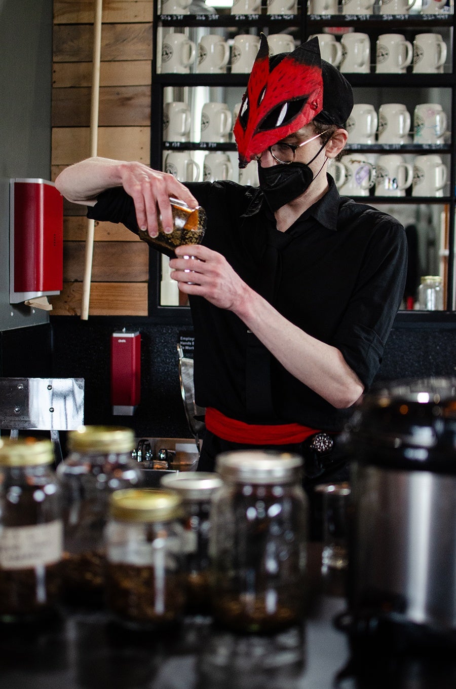 A barista wearing a fox mask prepares coffee.