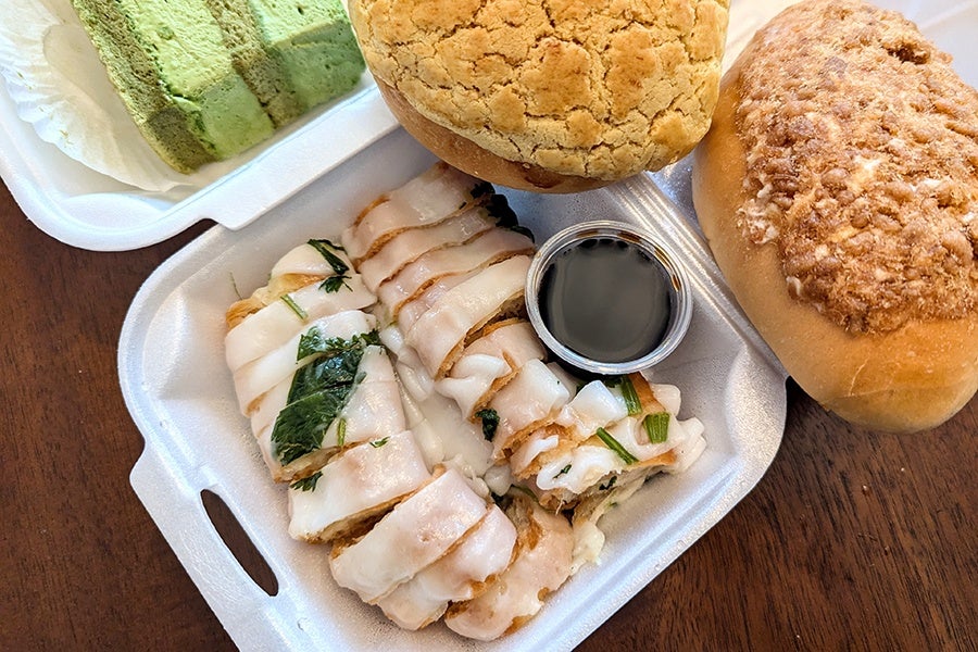 Overhead view of rice-noodle-wrapped fried dough bits, matcha cake, a pineapple bun, and a pork floss bun.
