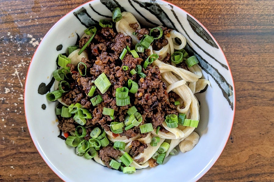 Top-down view of homemade hand-pulled noodles topped with a ground meat sauce and chopped scallions.