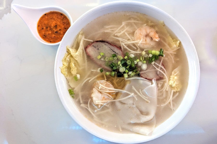 Overhead view of a bowl of chicken noodle soup with wontons and char siu pork.