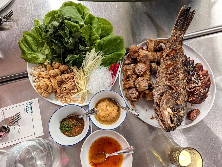 A spread of Lao food, including a crispy fried fish, sausage, fried pork and mushroom rolls, herbs, and sauces.