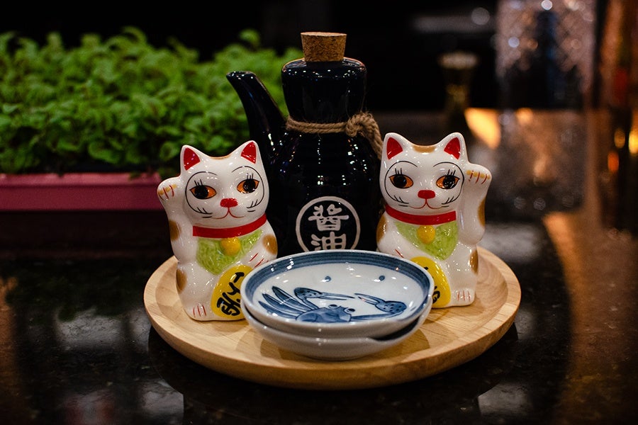 Two small Japanese waving cat ceramics sit next to a small jug of soy sauce and two small soy sauce plates decorated with crabs