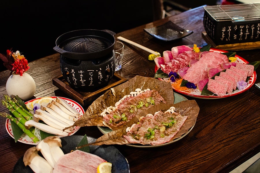 A restaurant table is covered with raw wagyu beef and accoutrements, and two small grills.