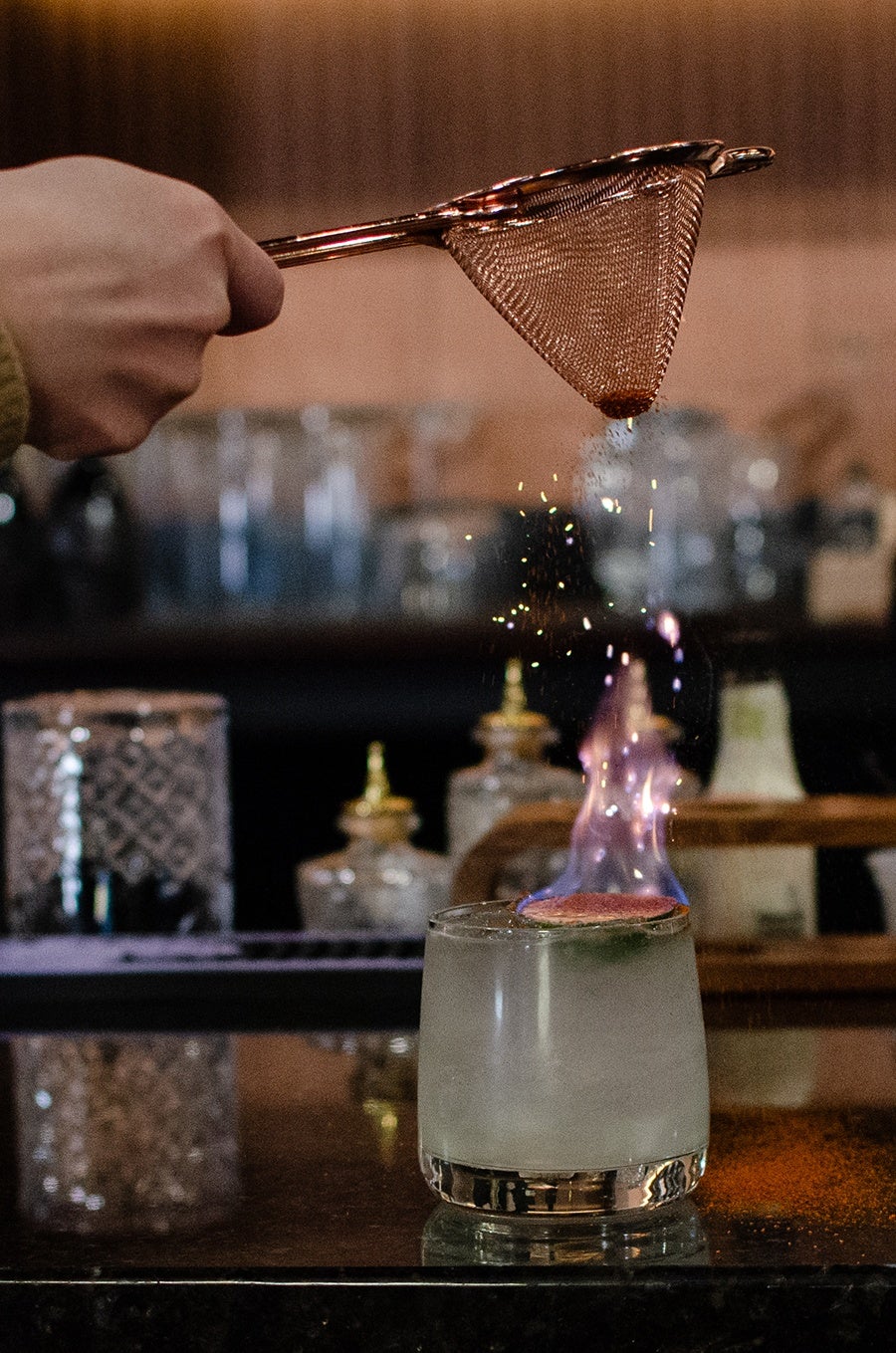 A lime atop a pale green cocktail is set on fire.