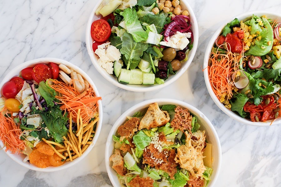Overhead view of four different salads and grain bowls on a white marble surface.