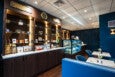 A small retail shop and restaurant features shelves of truffles, foie gras, and other luxury food items, and a couple small white marble tables with royal blue chairs, banquettes, and walls.