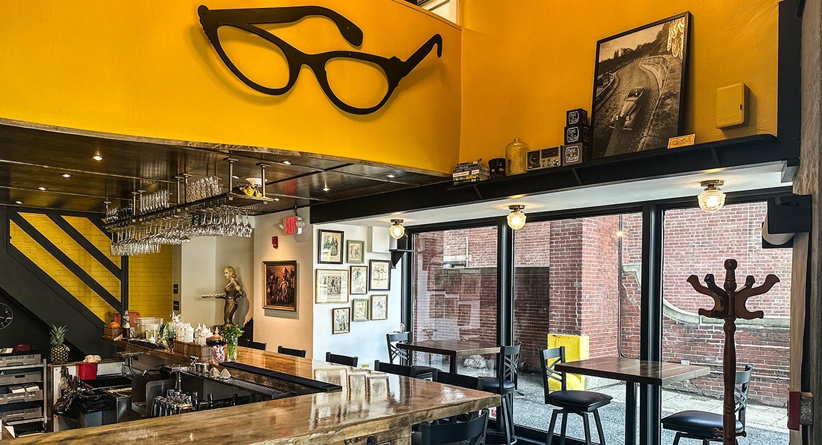 Interior of a bar with bright yellow walls, black-and-white checkered floors, and a big pair of decorative eyeglasses.