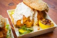 A thick, crispy fried chicken sandwich on a sesame bun is slathered with a ranch-like sauce, served with pickles and a charred lemon half.