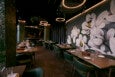 An empty restaurant dining room features dark green and gray tones and a large mural of white flowers.