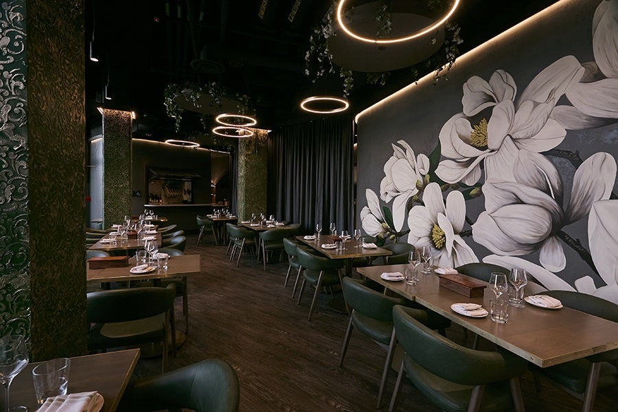 An empty restaurant dining room features dark green and gray tones and a large mural of white flowers.