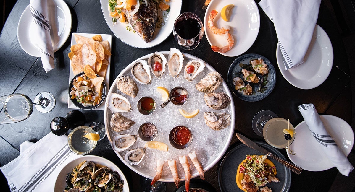 Overhead view of a table full of seafood, with a platter of oysters on the half shell in the center.