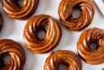 Overhead view of crullers lined up on a white surface, each with a light brown glaze.