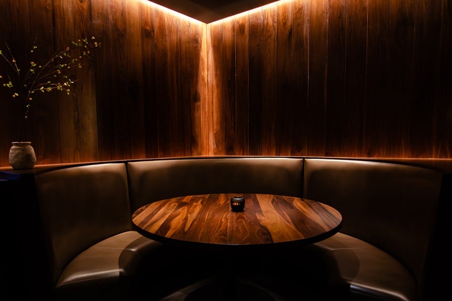 A round brown banquette with a wooden table, next to wood-paneled walls, inside a dimly lit restaurant.