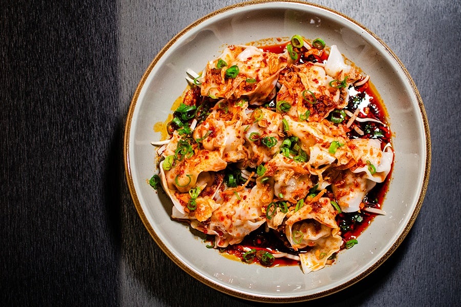Overhead view of a plate of wontons in a bright red sauce with scallions and crispy onion.