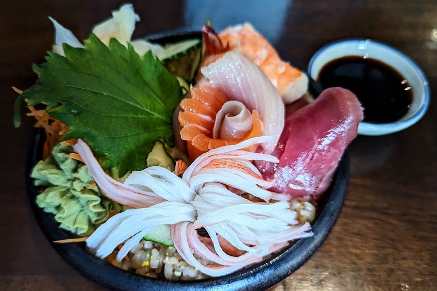 Closeup of a bowl of chirashi, various sliced raw fish over rice, with a shiso leaf and other garnishes.