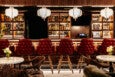 Red leather stools are lined up at a bar on a white-tiled floor.