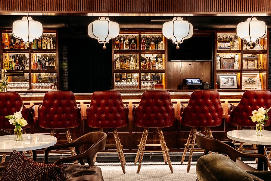 Red leather stools are lined up at a bar on a white-tiled floor.