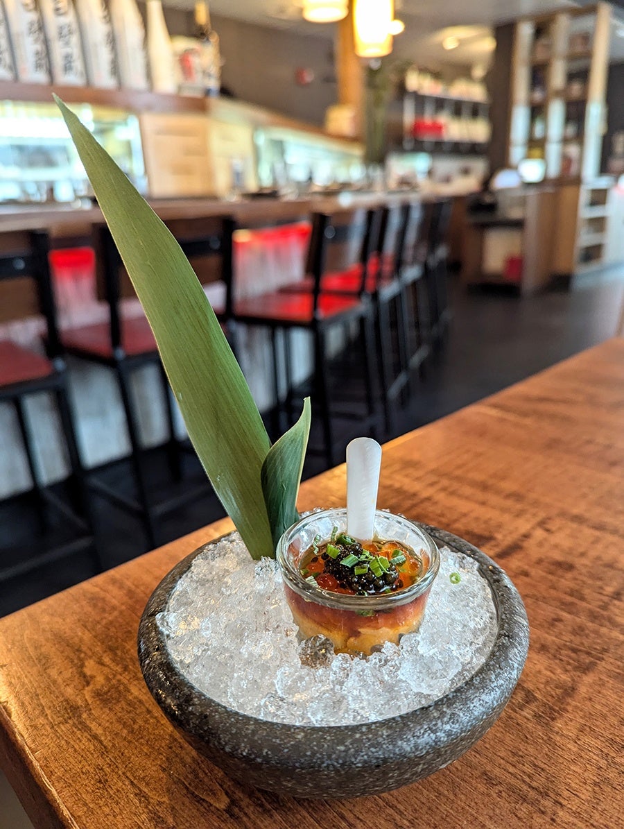 A shot glass of uni, ikura, and caviar is served on ice inside a Japanese restaurant.