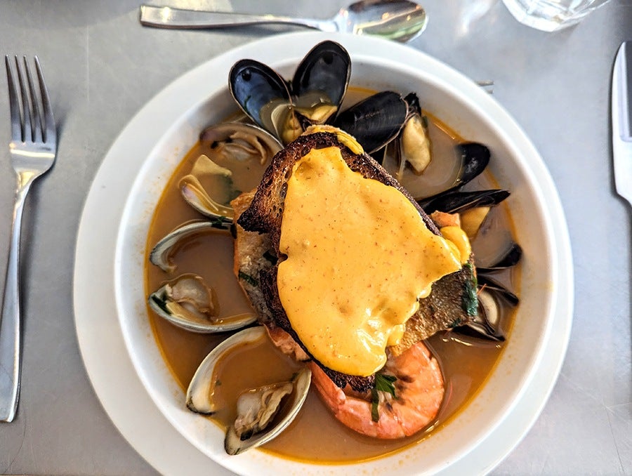 Overhead view of a shellfish-filled soup topped with a piece of bread with a thick layer of saffron aioli.