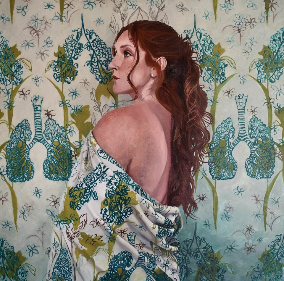 A woman with long, wavy auburn hair is shown in profile, looking to the left. She has a nose ring and small hoop earrings. Her bare back is exposed, and she is draped in a fabric with a botanical and anatomical lung pattern in green and blue tones. The background features a matching pattern of stylized lungs and floral elements in similar colors.