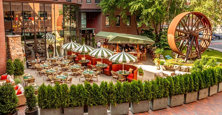 An Italian-inspired large restaurant patio with green-and-white -striped umbrellas and u-shaped red booths.
