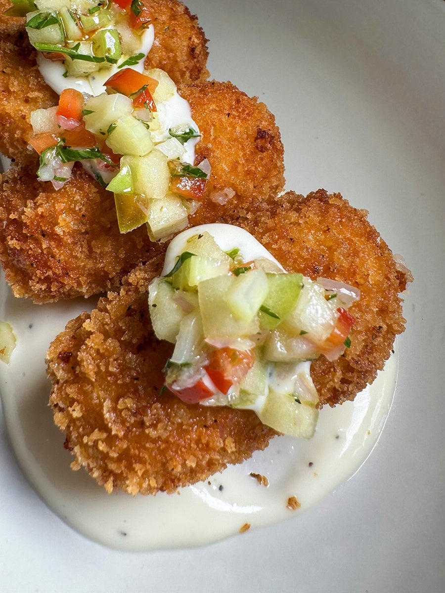 Closeup on crispy breaded ovals in a pool of white sauce, topped with chopped veggies.
