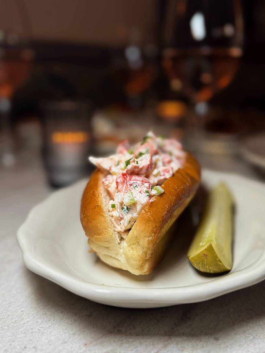 A lobster roll with mayo is accompanied by a pickle.