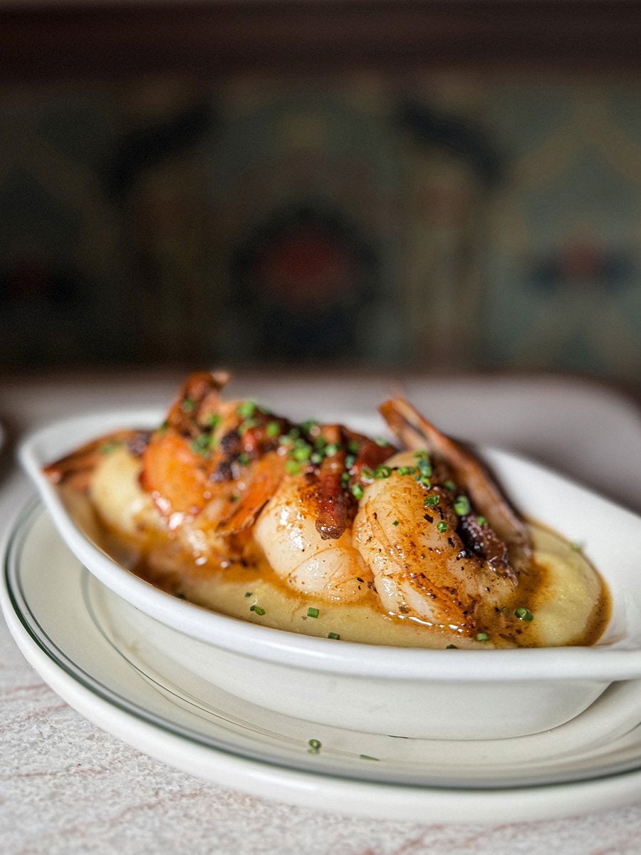 Three plump shrimps topped with chives sit on a bed of grits in an oval dish.