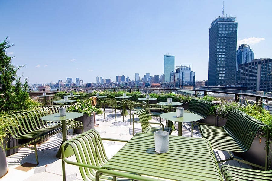 A rooftop patio features green outdoor furniture and skyline views of Boston.