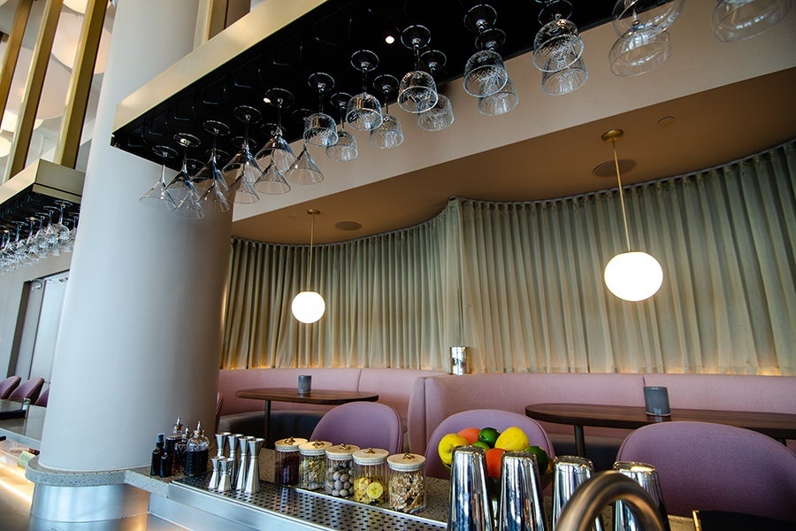 Interior of a bar with u-shaped pale pink booths with beige curtains hanging behind.