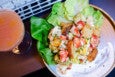 Overhead view of a salad with chunks of lobster, big croutons, bibb lettuce, and a swoosh of herby white sauce, next to a cocktail.