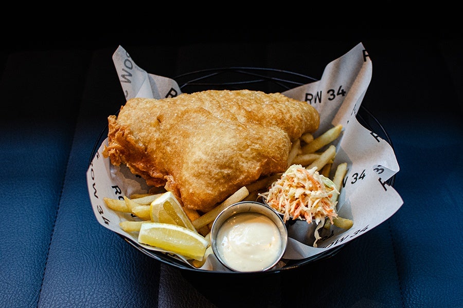 A big hunk of fried fish atop fries, garnished with slaw, lemon wedges, and a thick aioli.
